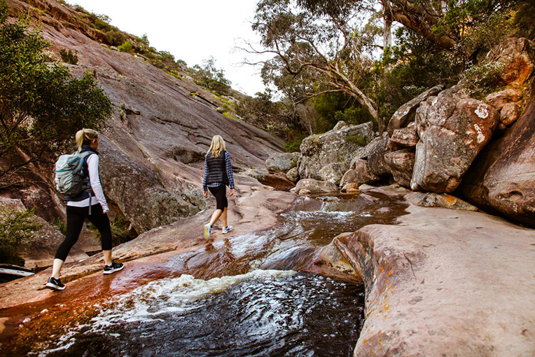 Two people hiking along a stream in the Grampians, Victoria.